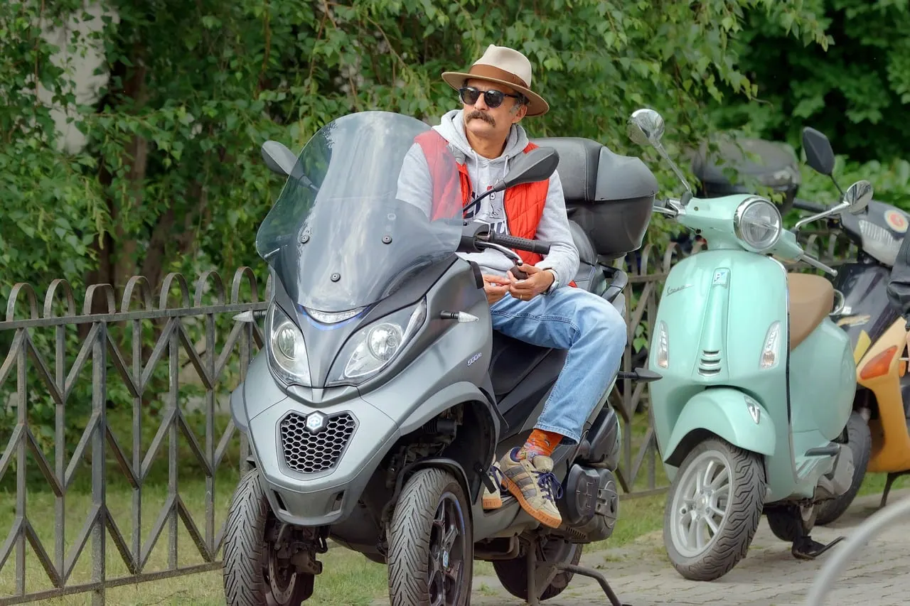 Homme assis sur un scooter à trois roues garé le long d’une grille