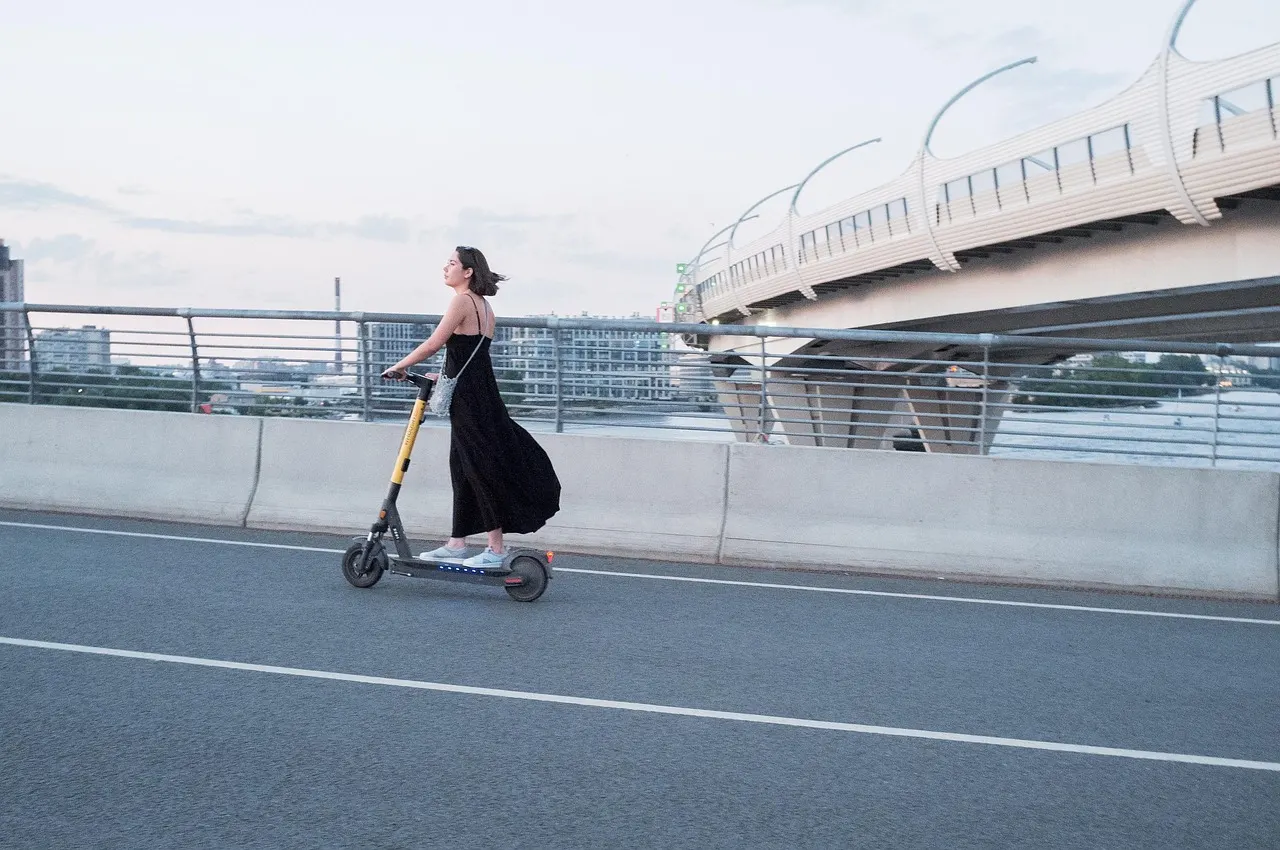 Femme en trottinette électrique sur une voie qui longe un pont
