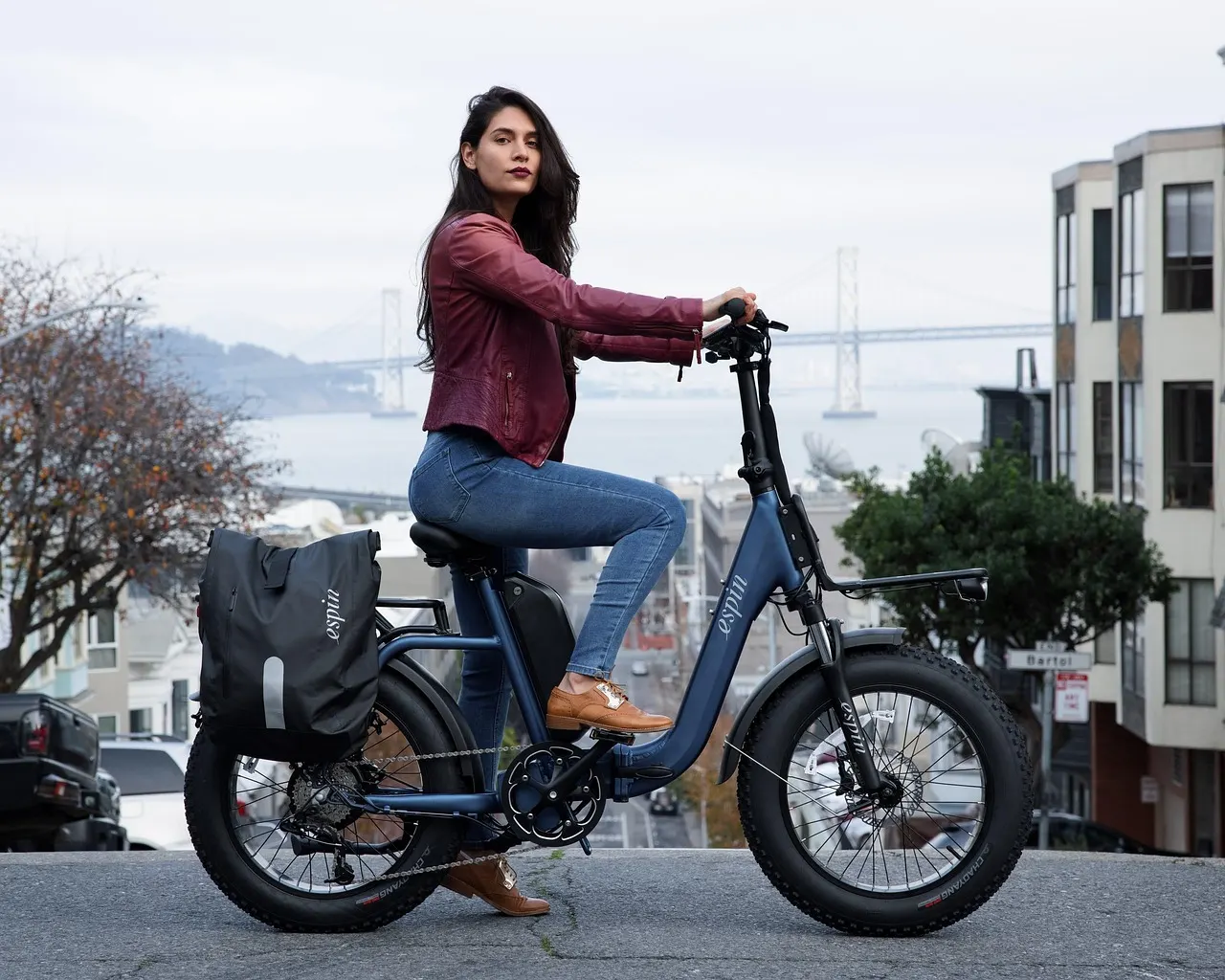 Femme à côté d’un vélo électrique à gros pneus, dans une rue en pente